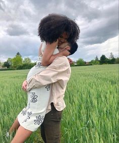 a woman holding a child in her arms while standing in the middle of a field