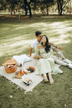 a man and woman sitting on top of a blanket next to each other in the grass