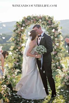 a bride and groom kissing in front of an arch of flowers