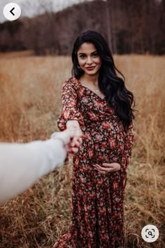 a pregnant woman holding the hand of a man in a field with tall brown grass