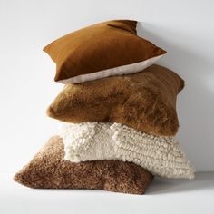 three pillows stacked on top of each other in different colors and sizes, one brown the other white