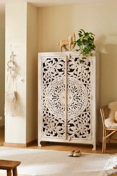 an ornate white cabinet in the corner of a living room with a plant on top