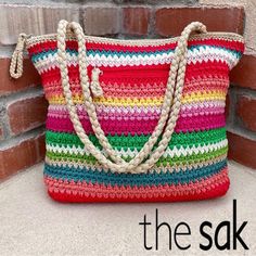 a multicolored crocheted bag sitting on top of a brick wall