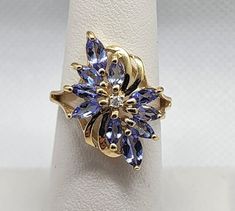 14K YELLOW GOLD TANZANITE & DIAMOND FLOWER RING  SIZE 5.5 RING WEIGHT 2.8 g Main Stone: Tanzanite Main Stone Shape: Marquise Main Stone Color: Lavender Main Stone Length: 5.5 mm Main Stone Width: 3 mm Number of Gemstones: 10 Secondary Stone: Diamond Number of Diamonds: 1 Formal Multi-stone Yellow Gold Flower Ring, Lavender Diamond, Diamond Flower Ring, Tanzanite Diamond, Diamond Flower, Flower Ring, Rings Statement, Stone Color, Statement Rings