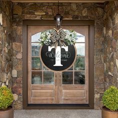 a welcome sign hanging on the front door of a house with two potted plants