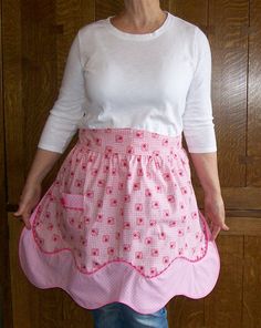 a woman wearing a pink and white polka dot apron with her hands in her pockets