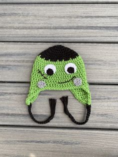 a crocheted green hat with eyes and nose is hanging on a wooden surface