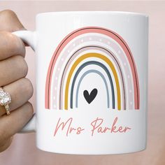 a person holding a coffee mug with a rainbow and heart on the inside, in front of a pink background