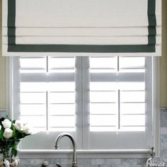 a kitchen sink under a window with white flowers in the vase on the counter top