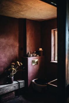 a bathroom with red walls and a toilet in the corner, next to a window