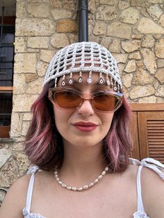 a woman with pink hair wearing sunglasses and a head piece in front of a stone building