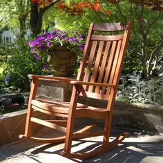 a wooden rocking chair sitting on top of a stone patio next to a potted plant