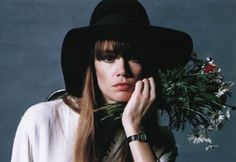 a woman with long hair wearing a black hat and holding a bouquet of flowers in front of her face