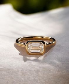 a gold ring with a baguette cut diamond on the side, sitting on a white cloth