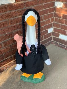 a duck statue is sitting on the ground next to a brick wall and wearing a black shirt