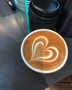 a cup of coffee on a table next to stacks of black plates and cups in the background