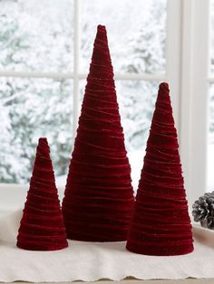 three small red christmas trees sitting on top of a white cloth covered table next to a window