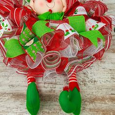 a red and green christmas mesh wreath with a teddy bear in it on a wooden surface