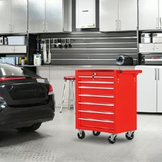 a red toolbox sitting next to a black car in a room with white cabinets