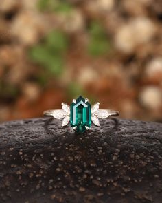 an emerald and diamond ring sitting on top of a rock