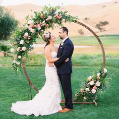 a bride and groom standing in front of an arch with flowers on it at their wedding