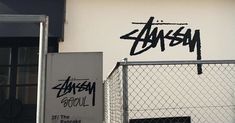 graffiti written on the side of a building near a chain link fence with a door