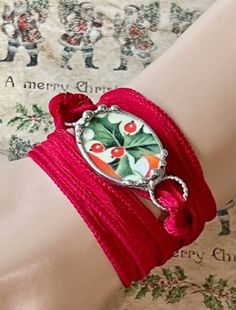 a close up of a person wearing a red bracelet with holly decorations on the wrist