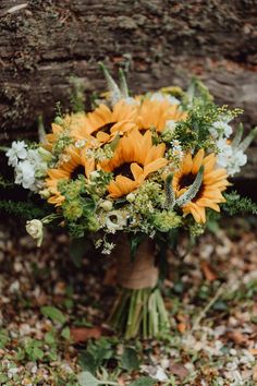 a bouquet of sunflowers and greenery is sitting on the ground next to a tree