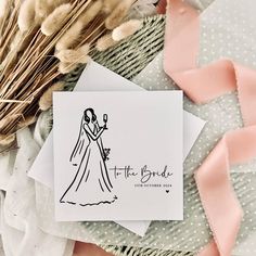 a wedding card with the bride and groom on it next to some dried flowers, feathers and ribbons