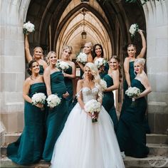 a group of women standing next to each other in front of a stone building holding bouquets