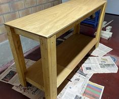 a wooden table sitting on top of a floor next to a pile of papers and magazines