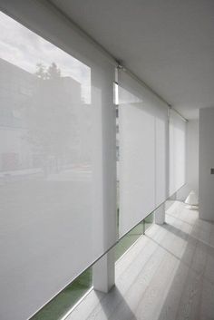 an empty room with white walls and wooden flooring is seen through the window blinds