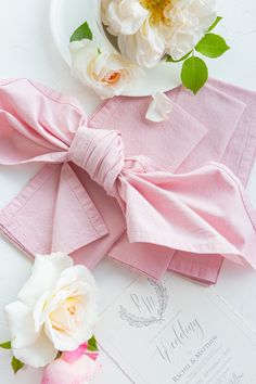 pink napkins with white flowers on top of them next to a plate and fork