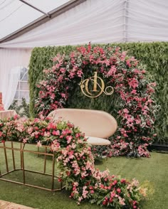 an outdoor ceremony area with pink flowers and greenery around the arch, decorated with gold monogrammed initials