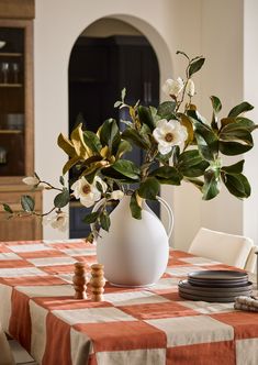 a white vase filled with flowers sitting on top of a checkered tablecloth covered table