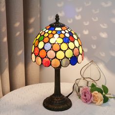 a colorful lamp sitting on top of a table next to a rose