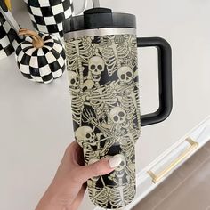 a person holding a coffee cup in their hand with skulls and bones on the side