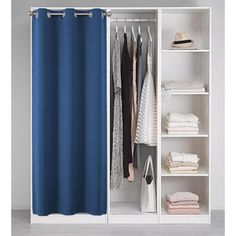 an open closet with blue curtains and clothes hanging on the shelves, next to a white bookcase