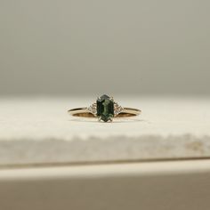 a ring with a green stone and two diamonds on it sitting on a white surface