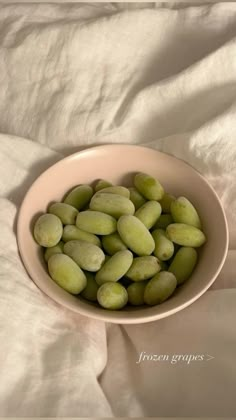 a bowl filled with green beans sitting on top of a white bed cover covered in sheets