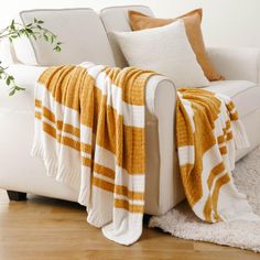 a white couch with a yellow and white blanket on top of it next to a potted plant