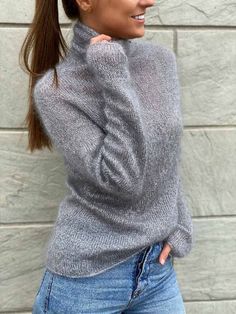 a woman with her hair in a ponytail wearing jeans and a gray turtle neck sweater