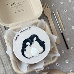 a couple of penguins sitting on top of a plate next to a fork and knife