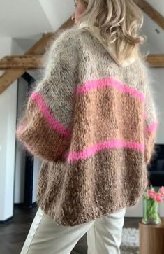 a woman wearing a sweater with pink and brown stripes on the side, standing in front of a fireplace