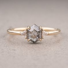 an engagement ring with three diamonds on the side and one stone in the middle, sitting on top of a gray surface