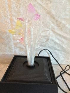 a glass vase with flowers in it on top of a black box next to a white wall