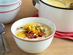 two white bowls filled with soup on top of a wooden table next to silverware