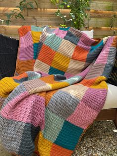 a multicolored blanket sitting on top of a wooden bench next to a potted plant