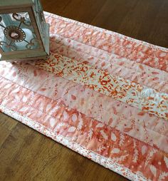 a clock sitting on top of a table next to a pink and orange piece of cloth