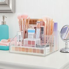 a clear container filled with makeup brushes and other items on top of a white counter